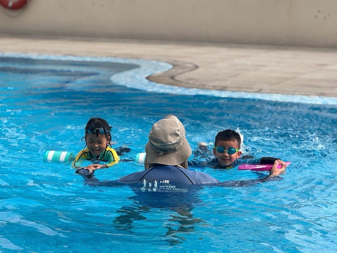 Instructor guiding two children with kickboards in the pool